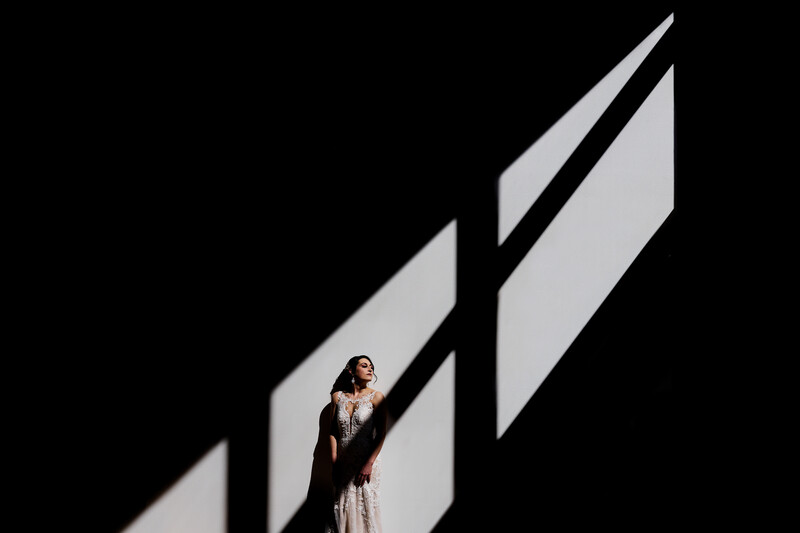 Woman standing in dramatic geometric shadow cast by angular black lines on dark background.