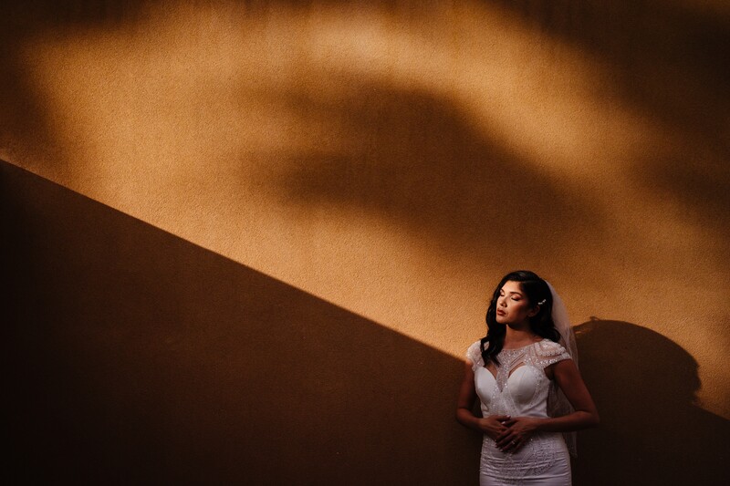 Woman in light-colored shirt standing against warm-toned wall with dramatic shadow cast across surface.