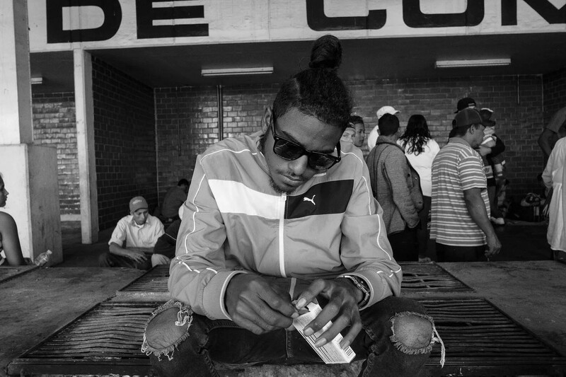 Person in sunglasses and white tracksuit jacket applying product to their hands in an indoor venue.