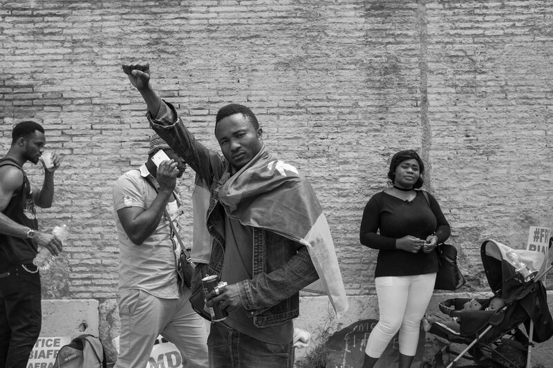 Man raising his fist at a public gathering against a brick wall backdrop.