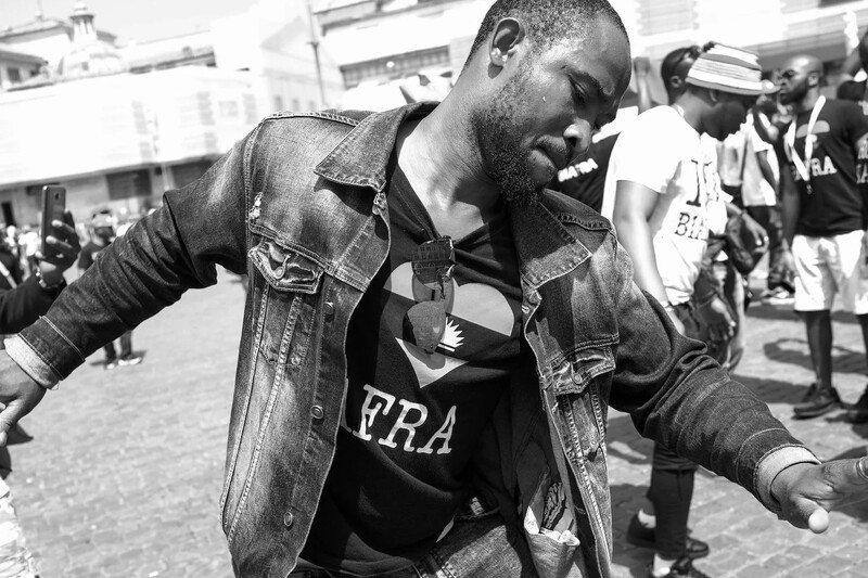 Man in denim jacket dancing outdoors with arms outstretched, captured in black and white.