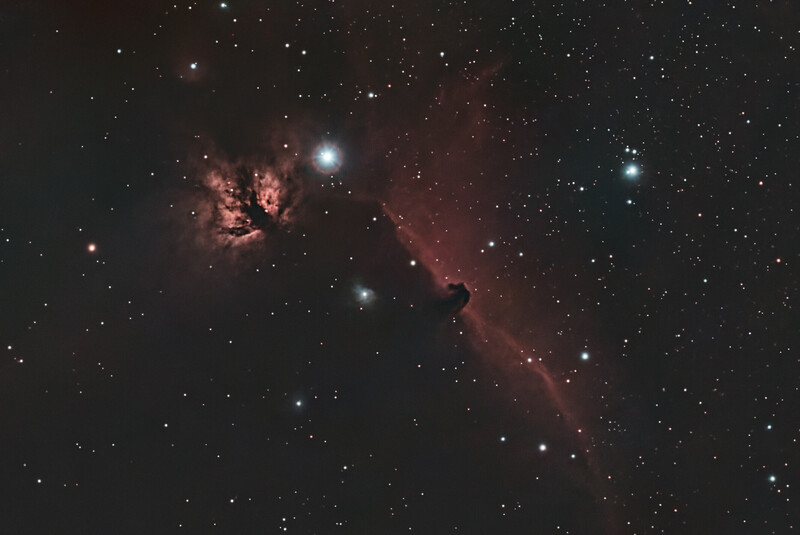 Deep-space astrophotography of a nebula with reddish emission clouds and scattered stars across dark space.