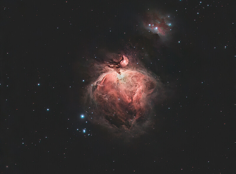 The Orion Nebula glowing in shades of pink and red against a starfield, with a smaller nebula visible above.