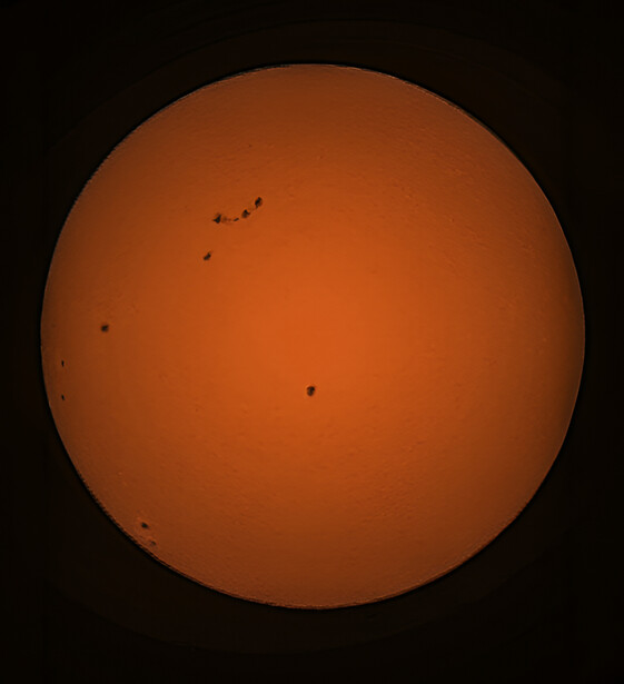 The Sun's disk with multiple sunspots visible across its orange surface against black space.