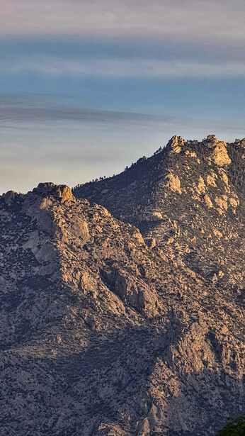 Rocky mountain peaks bathed in golden hour sunlight against a blue sky with clouds.