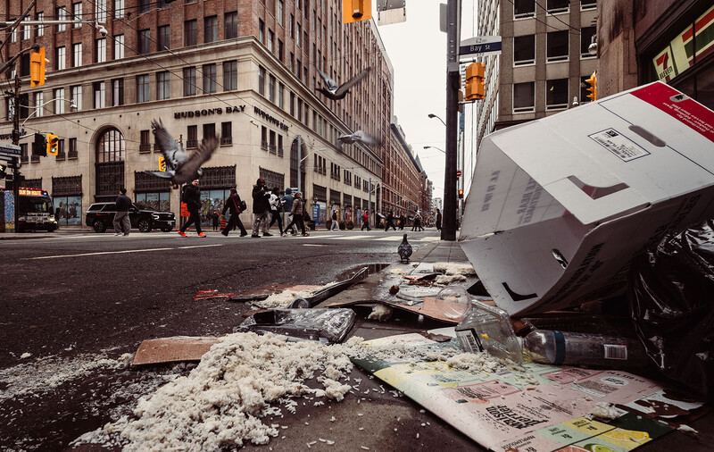 Scattered photographs and papers on an urban street with tall buildings and pedestrians in the background.