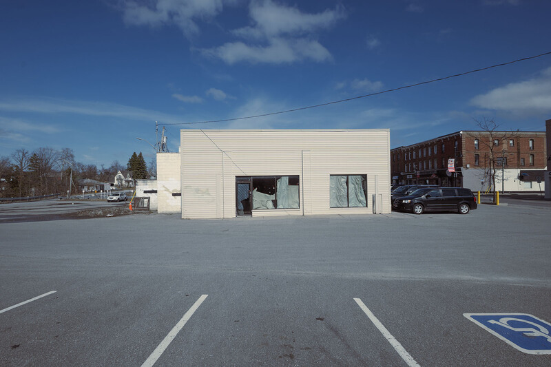 Minimalist white commercial building with large windows in empty parking lot on clear day.