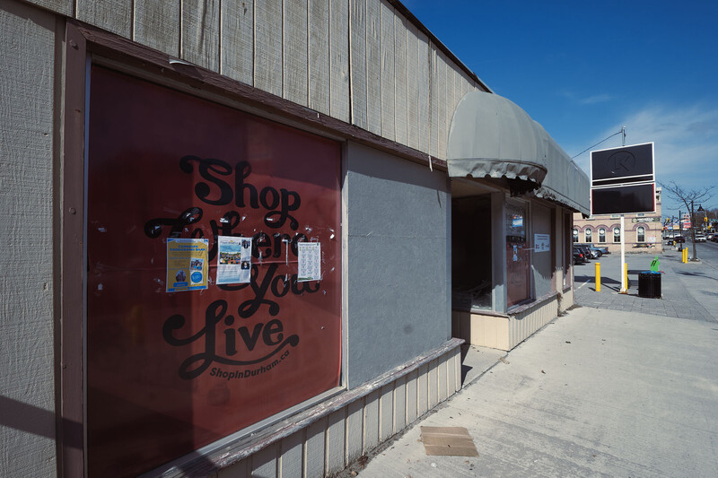 Storefront with red painted door and signage on weathered white brick building under clear blue sky.