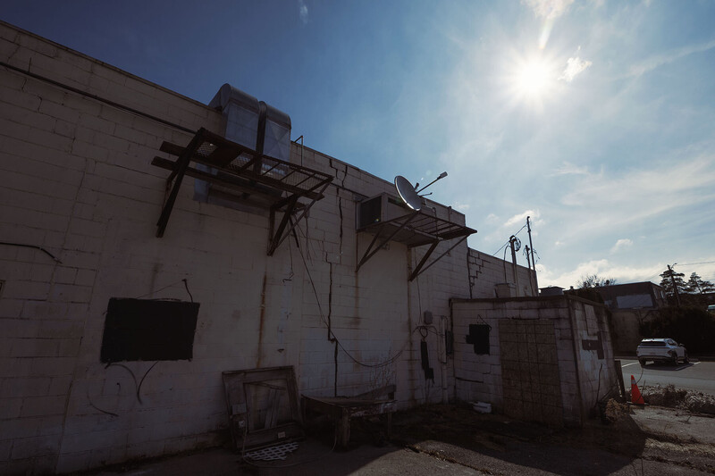 Deteriorating industrial building with metal framework and weathered white walls against blue sky.