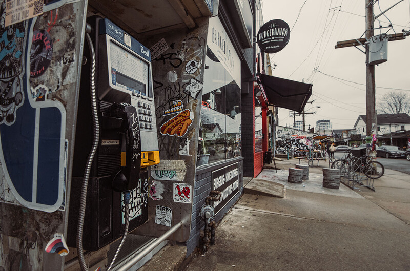 Street scene with weathered food truck covered in stickers and signage, parked along an urban sidewalk.