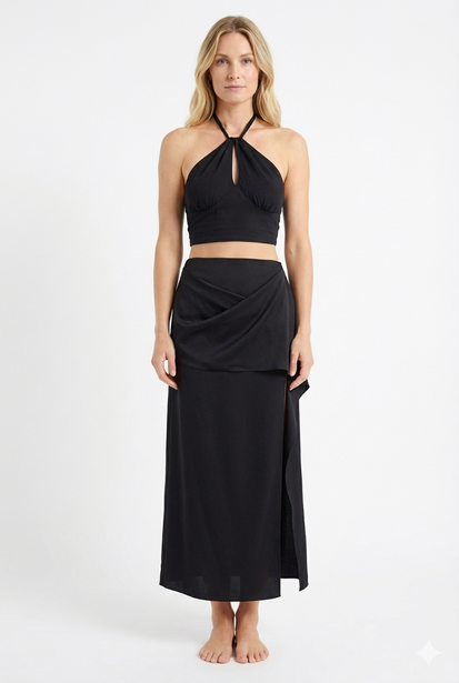 Woman in black halter crop top and midi skirt standing against neutral background.