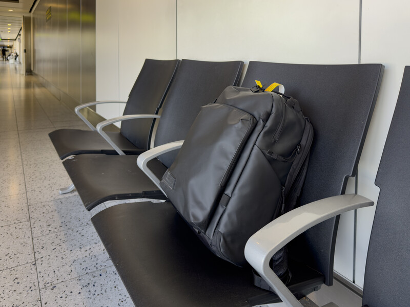 Black camera backpack resting on modern airport seating with metal armrests.
