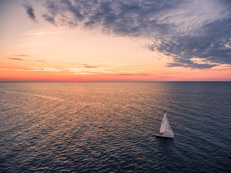 Sailboat with white sails on calm ocean water during golden hour sunset.