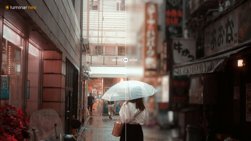 Person holding white umbrella walking through narrow urban alley lined with storefronts and neon signage.