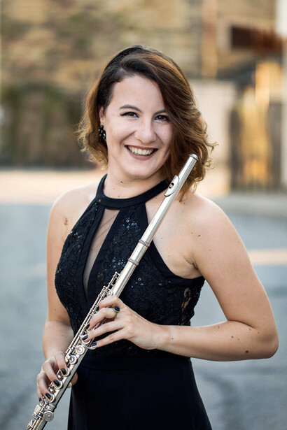 Woman in black halter dress holding a flute, smiling at camera outdoors.