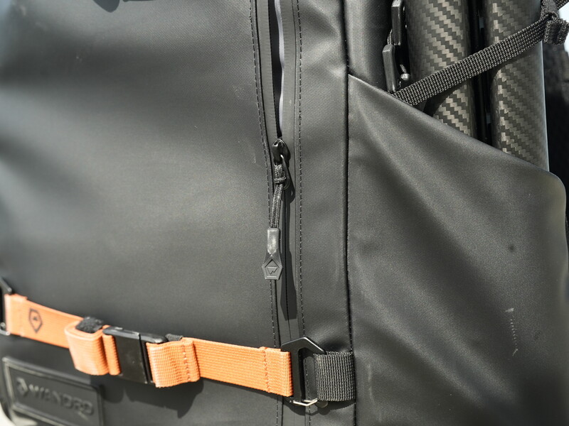 Close-up of a camera backpack with orange webbing straps and black weatherproof material.