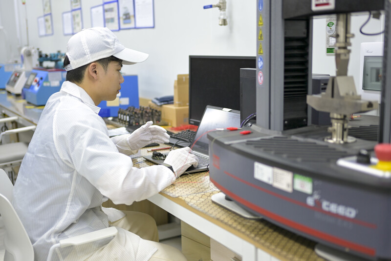 Technician in white cleanroom attire working at a workbench with electronic components and machinery.
