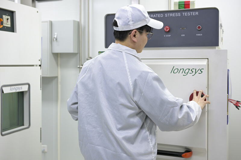 Technician operating a Longsys automated stress testing machine in a laboratory setting.
