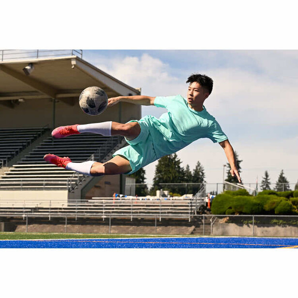 Soccer player mid-air performing an overhead kick with a ball in an outdoor stadium.