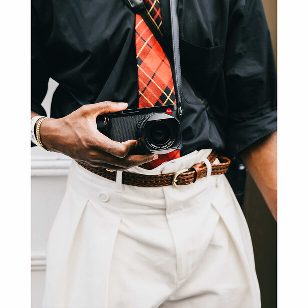 Person in black shirt and white trousers holding an empty black wallet.