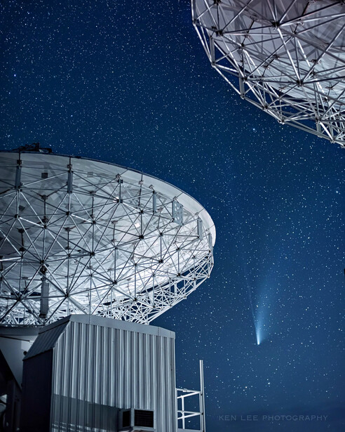 Large radio telescope dishes silhouetted against a starry night sky with a light beam visible.