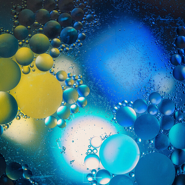 Abstract composition of colorful oil bubbles suspended in liquid with gradient lighting from yellow to blue.
