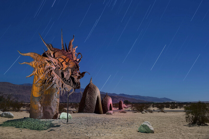 Sculptural art installation in desert landscape with star trails streaking across night sky.
