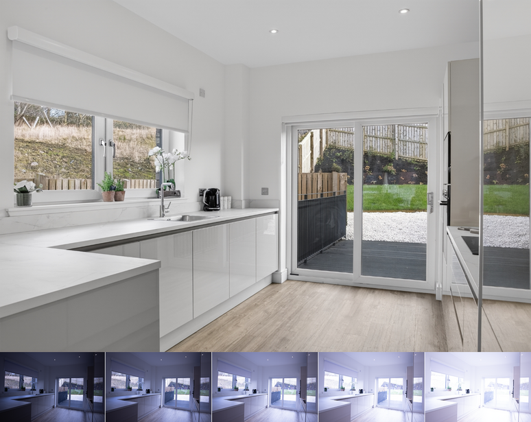 Modern white kitchen with island overlooking garden through glass doors, featuring minimalist design and natural light.