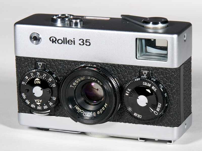Rollei 35 rangefinder camera with white top plate and black textured body, showing dual control dials and Tessar lens.