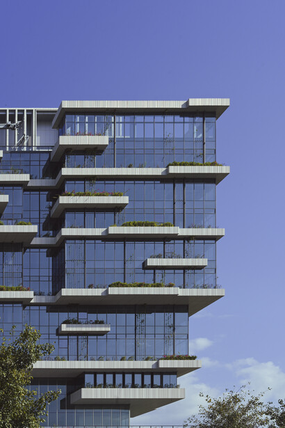 Modern residential tower with staggered balconies and blue-tinted glass facades against clear sky.