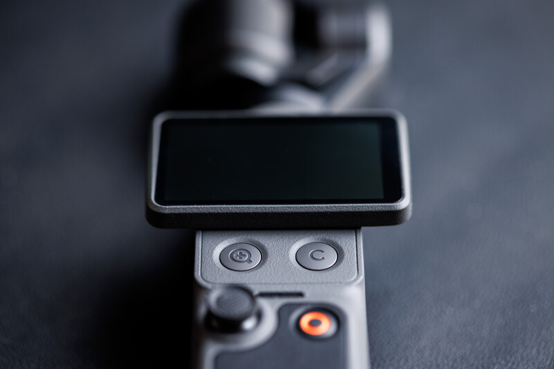 Close-up of a smartphone mounted on a gimbal stabilizer with dual control wheels and an orange button visible.
