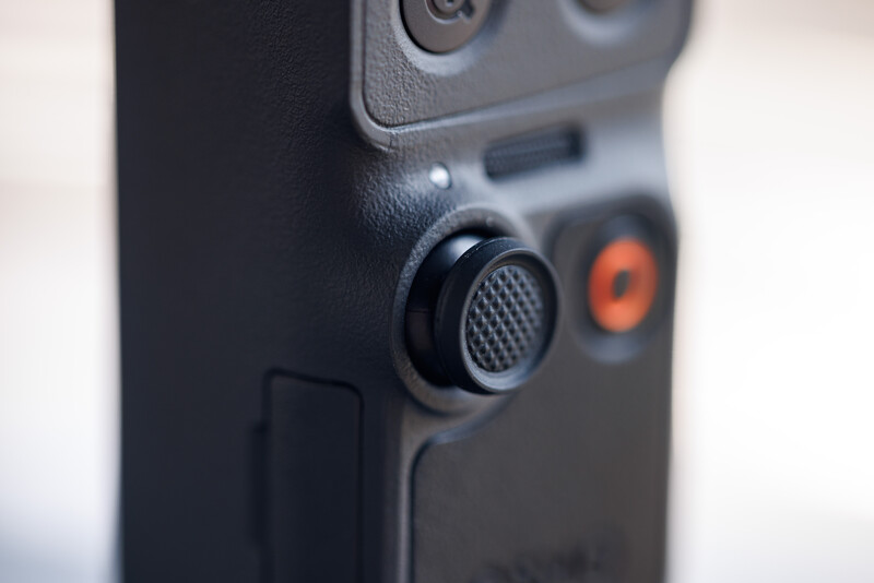 Close-up of a camera controller or gaming device showing a textured grip, analog stick, and orange accent buttons.