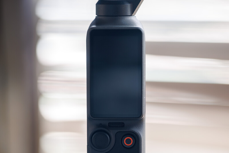 Close-up of a compact gimbal stabilizer with a smartphone mounted on top, featuring control buttons and a red recording indicator on the base.