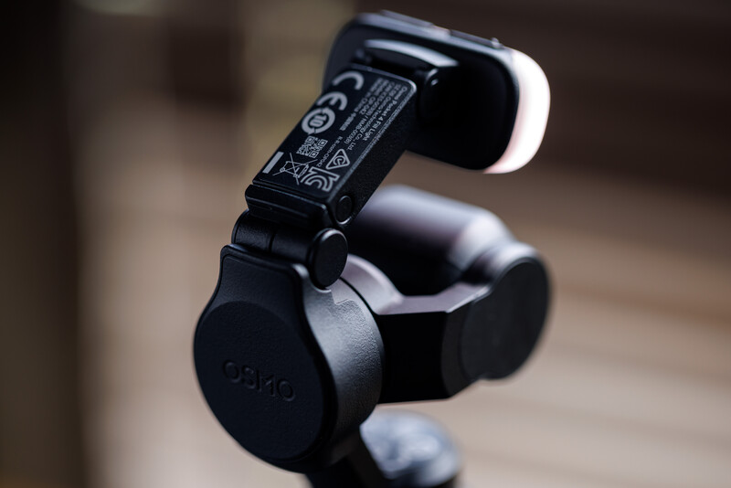 Close-up of a black gimbal stabilizer mounted on a tripod head, showing mechanical joints and adjustment mechanisms.