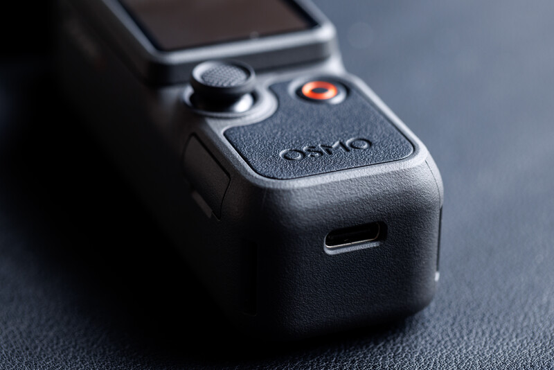 DJI drone remote controller with textured grip, control stick, and orange accent button on dark surface.