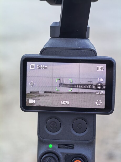 Drone controller with mounted smartphone displaying live video feed of a landscape with train or vehicle on tracks.
