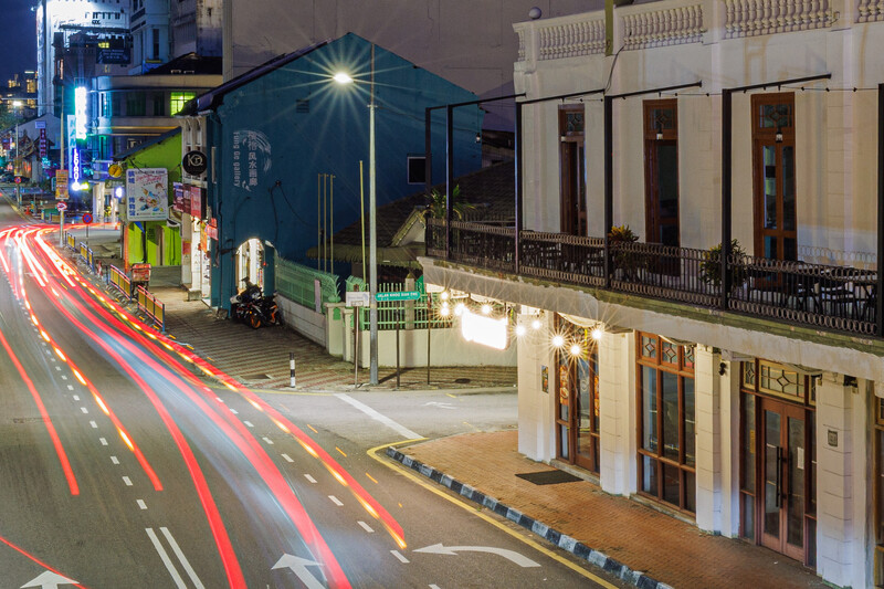 Night urban street scene with light trails from vehicle traffic flowing past colonial architecture.