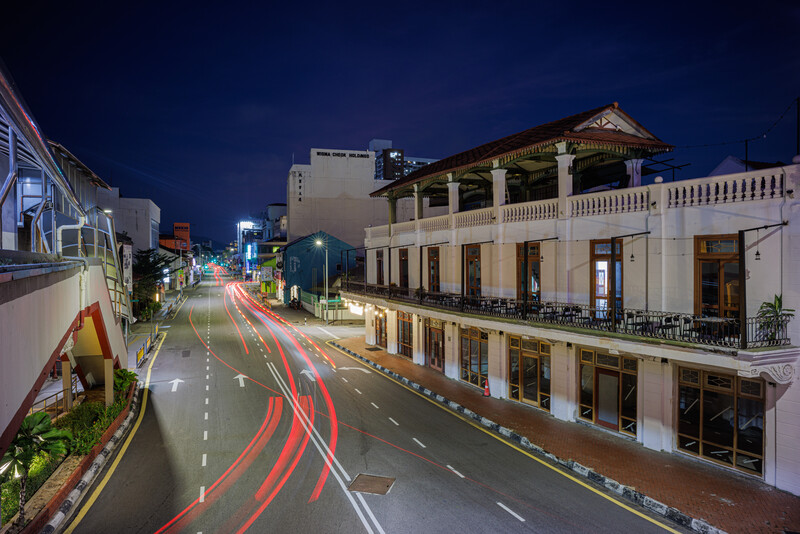Nighttime street scene with colonial-style buildings and light trails from vehicle traffic.