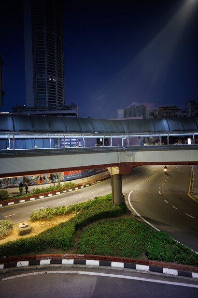 Modern elevated highway overpass at night with blue-lit underpass and city skyline in background.