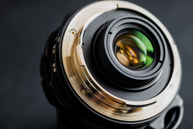 Close-up of a camera lens showing internal glass elements and brass focusing mechanism against a dark background.