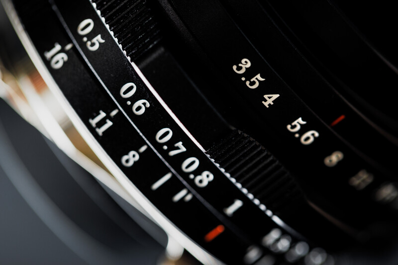 Close-up of camera lens focus and aperture rings showing depth of field markings and f-stop numbers.