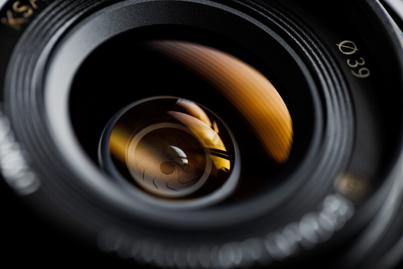 Close-up of a camera lens aperture with golden-brown diaphragm blades against black barrel.