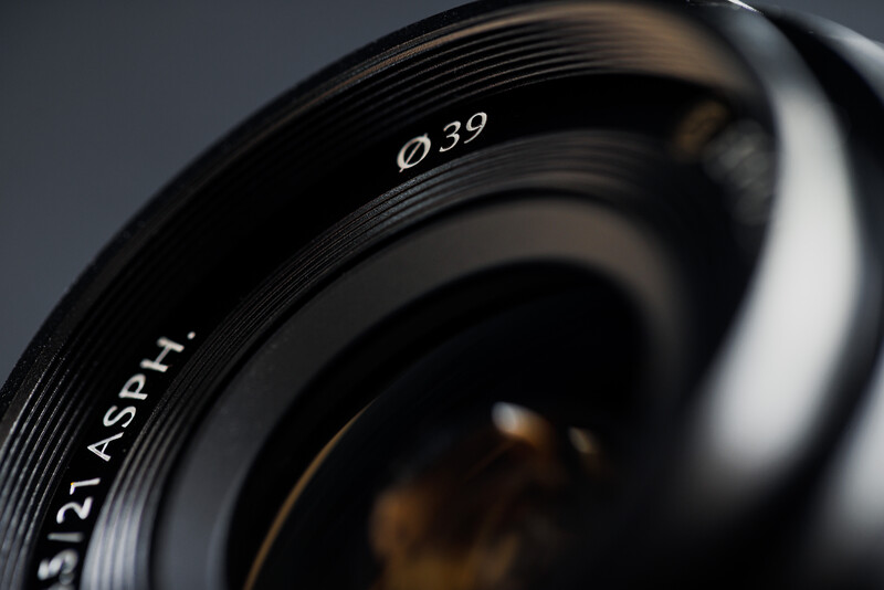 Close-up of a camera lens barrel showing diameter marking Ø39 and Asph lens designation with grooved focusing ring.