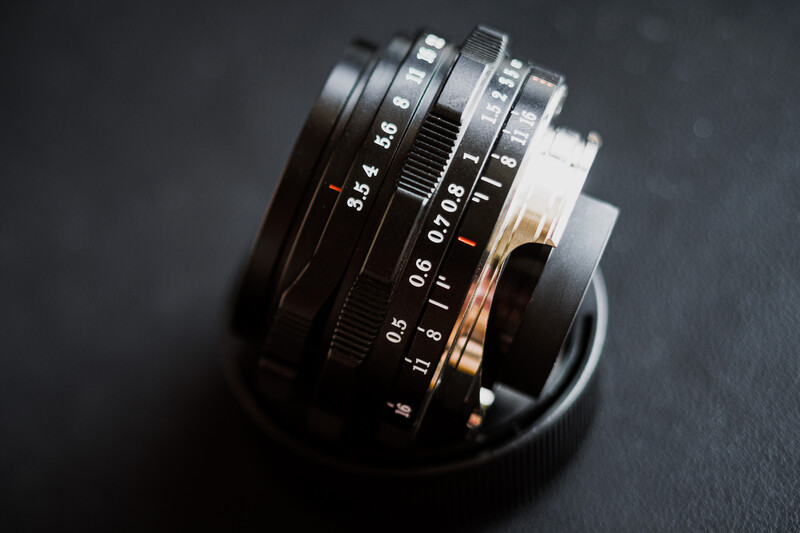 Collection of vintage manual focus lenses with aperture and focus rings arranged in a circular display against a dark surface.