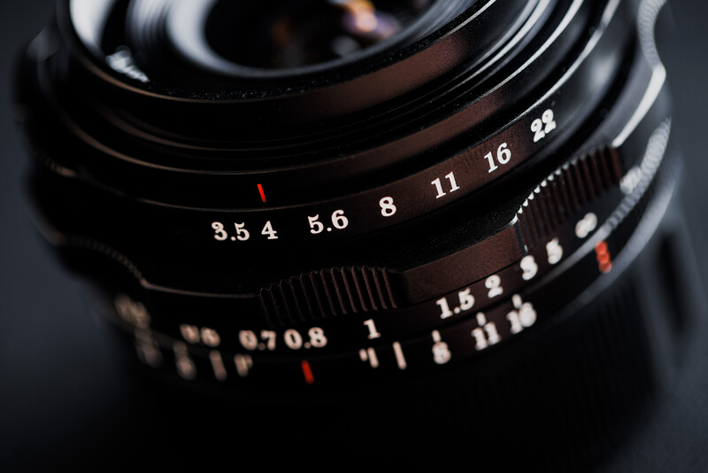 Close-up of vintage camera lens barrel showing aperture f-stops and depth-of-field scale markings.