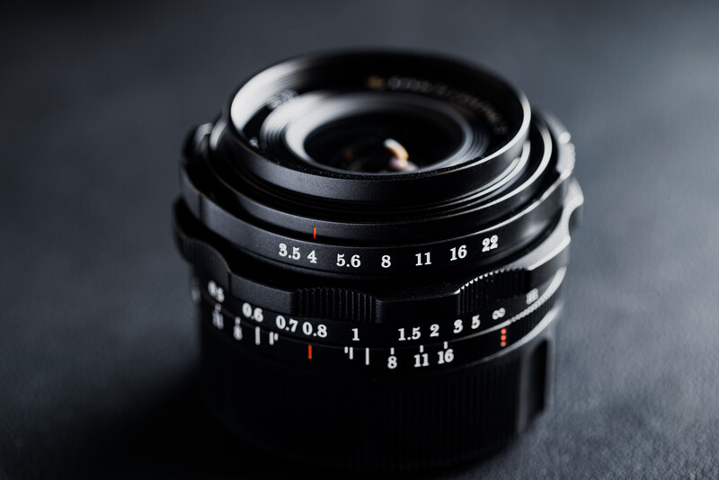 Vintage manual focus lens with aperture and focus distance scales on dark surface.