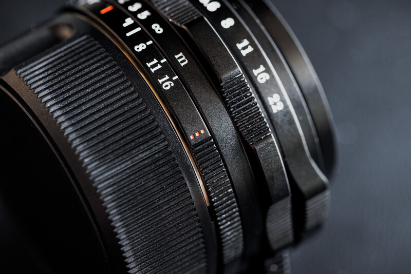 Close-up of camera lens barrels showing focus rings and depth-of-field markings on black background.