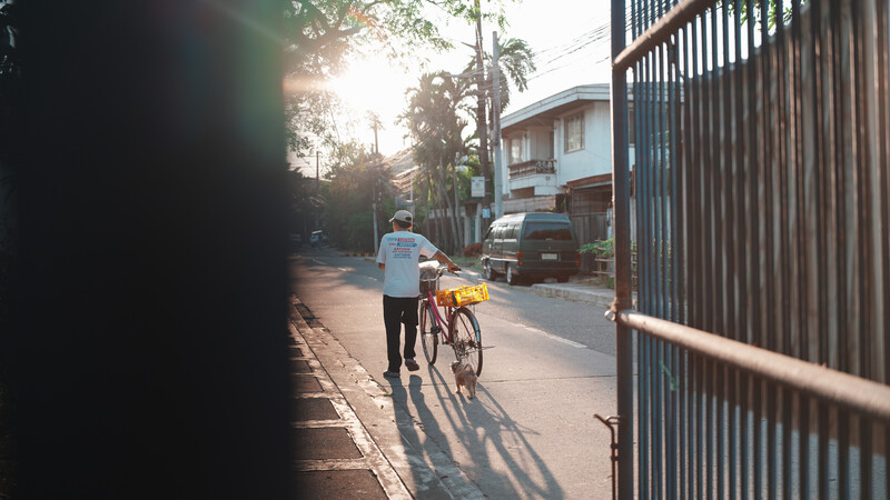 Person jogging while pushing a bicycle along a tree-lined residential street at golden hour.