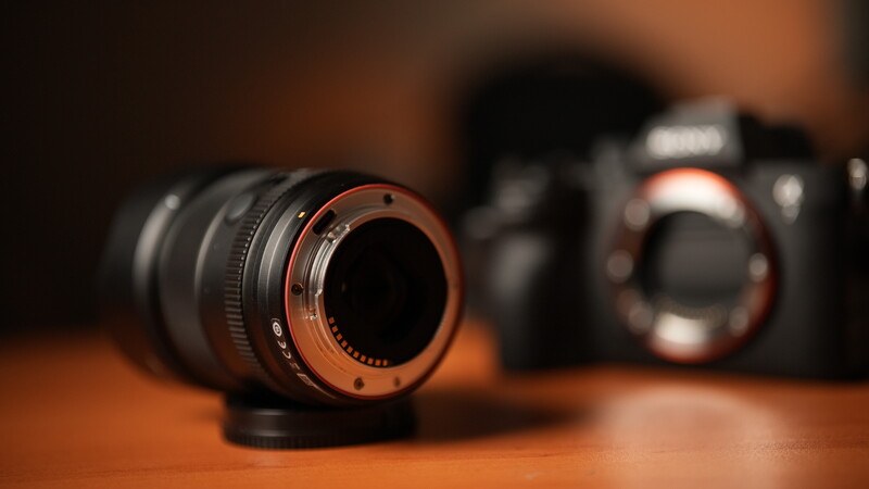 Camera lens with copper-colored rear element in sharp focus, with blurred camera body in background.