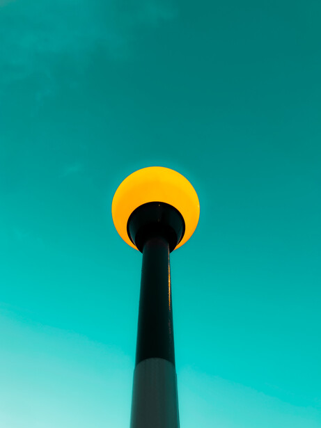 A tall dark structure silhouetted against a turquoise sky with a large yellow circular form at its top.